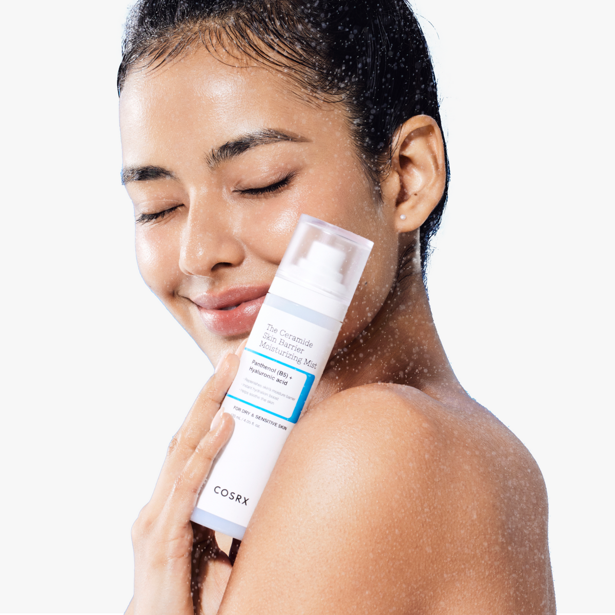 Model with eyes closed and relaxed expression spraying COSRX The Ceramide Skin Barrier Moisturizing Mist; ultra-fine mist droplets illustrate immediate cooling relief and deep hydration that calms dry, sensitive skin and refreshes makeup, clinically proven to deliver moisture penetration across 12 layers of the stratum corneum for lasting barrier support.