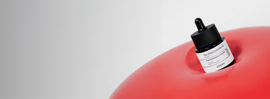 Monochrome banner featuring COSRX The Niacinamide 15 Serum and The Hyaluronic Acid 3 Serum bottles beside a glass of water; text reads ‘High-Strength Total Trouble Care’, emphasizing all-in-one acne treatment and sebum control for clearer, balanced skin.