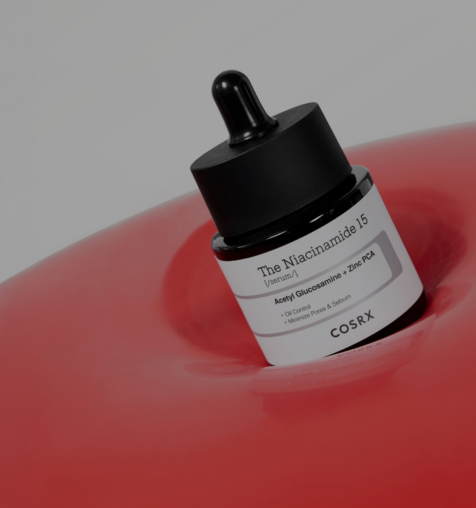Monochrome banner featuring COSRX The Niacinamide 15 Serum and The Hyaluronic Acid 3 Serum bottles beside a glass of water; text reads ‘High-Strength Total Trouble Care’, emphasizing all-in-one acne treatment and sebum control for clearer, balanced skin.