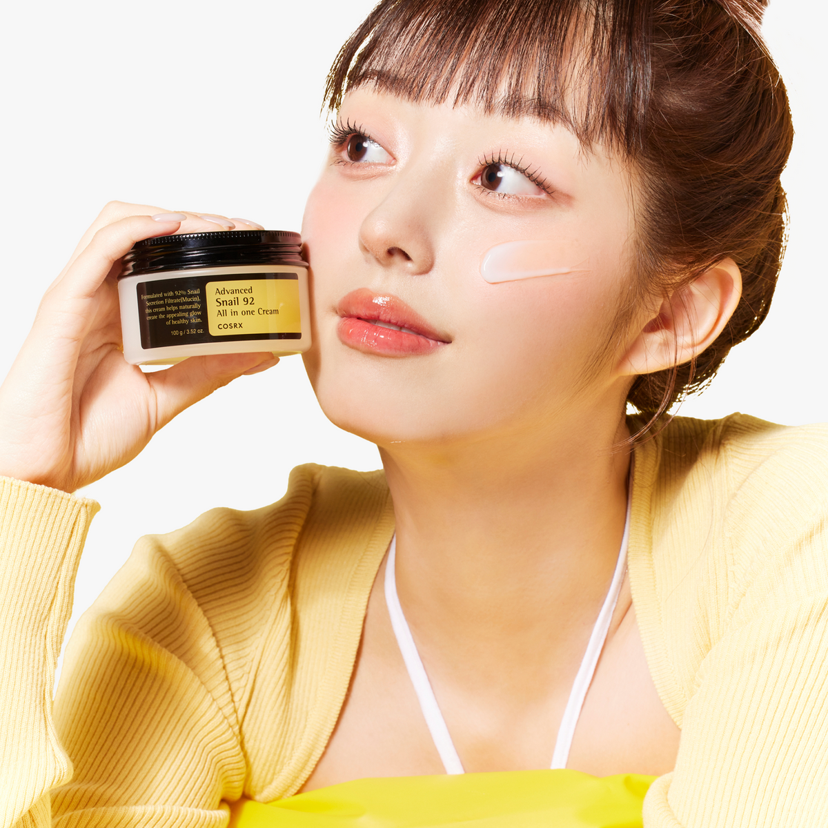 Model applying COSRX Advanced Snail 92 All In One Cream from jar, revealing smooth, dewy skin finish. Korean daily moisturizer with 92% snail mucin, clinically measured to reduce redness by 82.73% using the Antera 3D system, supporting hydration, anti-aging care, and a visibly healthier, glowing complexion.